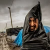 Một người nhập cư lấy túi rác làm áo mưa đi qua con đường đầy bùn đất tại tại tị nạn ở Calais. (Ảnh: AFP)