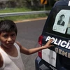 Một cậu bé Mexico đứng sau chiếc xe cảnh sát có dán yết thị truy nã trùm El Chapo (Nguồn: DM)