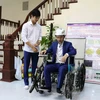 Em Nguyễn Hữu Thành Đạt (bên trái) và Nguyễn Công Khánh thử nghiệm xe lăn leo cầu thang điều khiển bằng cử chỉ của đầu, giọng nói và điện thoại thông minh. (Ảnh: Thanh Thương/ TTXVN)