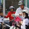 Phụ huynh đội mũ bảo hiểm cho trẻ khi tham gia giao thông. (Ảnh: TTXVN)