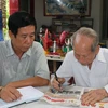 Ông Nguyễn Văn Thọ (phải) và con trai Nguyễn Thanh Hà đọc thông tin ở mục tìm thân nhân liệt sỹ trên báo. (Ảnh: Hữu Chí/TTXVN)