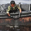 Một công nhân múc dầu ở cảng Đại Liên, Liêu Ninh (Trung Quốc) do vỡ đường ống dẫn dầu, khiến 1.500 tấn dầu thô tràn vào nước. (Nguồn: Techinsider)