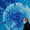 Người dân đeo khẩu trang đi ngang qua hình ảnh minh họa cho virus SARS-CoV-2. (Ảnh: Reuters) 