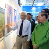 Ông Trần Khánh Chương, Chủ tịch Hội Mỹ thuật Việt Nam (áo trắng) giới thiệu tranh với Bộ trưởng Thông tin-Văn hóa và Du lịch Lào, ông Bosengkham Vongdala. (Ảnh: Phạm Kiên/TTXVN)