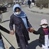 Một phụ nữ dắt hai con nhỏ đeo khẩu trang chống COVID-19 đi bộ dọc theo một con đường ở Kabul ngày 18/3. (Nguồn: AFP)