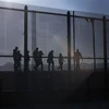 Lực lượng bảo vệ biên giới Mỹ (trái) bắt giữ người di cư trái phép tại biên giới Mexico - Mỹ, ở El Paso, Texas, ngày 21/12/2022. (Ảnh: AFP/TTXVN)