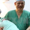 Giáo sư, tiến sỹ Nguyễn Viết Tiến, Thứ trưởng Bộ Y tế - người trực tiếp thực hiện phẫu thuật lấy thai cho ca mang thai hộ đầu tiên tại Bệnh viện Phụ sản Trung ương - bế bé gái mới sinh. (Ảnh: Dương Ngọc/TTXVN)