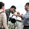 Anh Đặng Vũ Tuấn Sơn (phải) hướng dẫn các bạn trẻ quan sát bầu trời qua kính thiên văn. (Ảnh: Doãn Đức/Vietnam+)