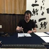 Ông Tadashi Ito viết thư pháp bằng mực Suzukazumi. (Ảnh: Nguyễn Tuyến/Vietnam+)