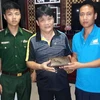 Thuyền trưởng Đinh Khắc Thương (áo xanh, bên phải) trả lại ví tiền cho du khách. (Ảnh: TTXVN phát)