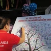 Các tình nguyện viên tham dự buổi lễ cùng ký tên ủng hộ việc chống kỳ thị người nhiễm HIV. (Ảnh: Đinh Hằng/TTXVN)