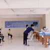 Các sinh viên Việt Nam nộp giấy khai tên họ, số điện thoại và khai lịch sử đi lại cho các nhân viên y tế Lào trước khi lấy mẫu xét nghiệm. (Ảnh: Phạm Kiên/Vietnam+)