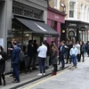 Người dân xếp hàng mua đồ bên ngoài một cửa hàng ở London (Anh). (Ảnh: AFP/TTXVN)