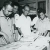 Nhà báo Bùi Đình Túy (người đeo kính) hướng dẫn phóng viên Nhật Bản Konishi xem các bộ ảnh triển lãm do TTXVN biên soạn, tháng 7/1964. (Nguồn: TTXVN)