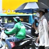 Người dân sử dụng ô, quần áo chống nóng khi phải di chuyển ngoài trời. (Ảnh: Hoàng Hiếu/TTXVN)