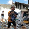 Các em nhỏ thu nhặt đồ đạc sót lại trong đống đổ nát của ngôi nhà bị phá hủy sau cuộc tấn công của Israel vào thành phố Rafah, Dải Gaza ngày 1/5.(Ảnh: THX/TTXVN)