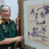 Họa sỹ Lê Duy Ứng và phiên bản của bức chân dung Bác Hồ vẽ bằng máu. (Ảnh: Minh Thu/Vietnam+)