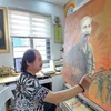 Họa sỹ Trần Xuân Phúc bên tác phẩm khắc họa Chủ tịch Hồ Chí Minh với lực lượng vũ trang. (Ảnh: Minh Thu/Vietnam+)