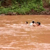 Phụ huynh và giáo viên nguy hiểm vượt dòng nước dữ đưa học sinh qua suối đến trường. (Ảnh: Việt Hoàng/TTXVN)