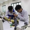 Phạm Đức Linh và Nguyễn Văn An cùng nhau nghiên cứu sản phẩm Cánh tay robot cho người khuyết tật liệt cơ tay toàn phần. (Ảnh: Thanh Thương/TTXVN) 