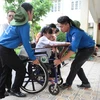 Thí sinh khuyết tật Lê Thị Hà An được các bạn sinh viên tình nguyện nhiệt tình hỗ trợ đến dự thị. (Ảnh: Minh Sơn/Vietnam+)