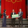 Ông Nghiêm Xuân Thành - Chủ tịch HĐQT Vietcombank trao biển tượng trưng tặng thuyền máy cho ông Võ Văn Bình và học bổng cho cháu Võ Nhật Thanh. (Ảnh: Vietnam+)