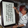 Nghệ nhân Lê Văn Kinh bên các bức tranh thêu bằng tiếng Việt và tiếng Hán (Trung Quốc). (Ảnh: Quốc Việt/TTXVN)