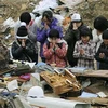Các trẻ em Nhật Bản cầu nguyện cho những người đã mất trước đống đổ nát do sóng thần gây ra (Nguồn Internet)