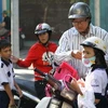 Trẻ em được phụ huynh đội mũ bảo hiểm khi tham gia giao thông bằng xe máy. (Ảnh: Phương Vy/TTXVN)