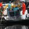 Công nhân thu gom dầu tràn do vụ nổ ống dẫn dầu. (Nguồn: china.org.cn)