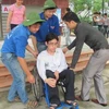 Sinh viên tình nguyện giúp Hoàng khiêng xe lăn. (Ảnh: Phạm Mai/Vietnam+)