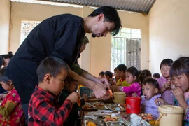 Ca sỹ Đen Vâu cẩn thận bóc tôm cho học sinh vùng cao trong bữa ăn bán trú. (Ảnh: PV/Vietnam+)