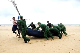 Cán bộ, chiến sỹ Đồn Biên phòng Lý Hòa (Bộ đội Biên phòng Quảng Bình) giúp ngư dân xã Đức Trạch, huyện Bố Trạch, tỉnh Quảng Bình đưa thuyền lên bờ tránh trú. (Ảnh: TTXVN phát)