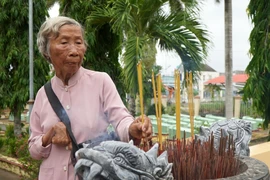 Bà Đặng Thị Bảy thắp hương cho đồng đội đang yên nghỉ tại Nghĩa trang liệt sĩ xã Long Hưng A. (Ảnh: Nhựt An/TTXVN)