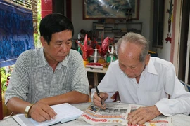 Ông Nguyễn Văn Thọ (phải) và con trai Nguyễn Thanh Hà đọc thông tin ở mục tìm thân nhân liệt sỹ trên báo. (Ảnh: Hữu Chí/TTXVN)