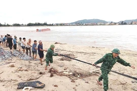 Cán bộ, chiến sỹ Đồn Biên phòng Cửa khẩu Cảng Gianh (Bộ đội Biên phòng Quảng Bình) và người dân cùng các lực lượng liên quan triển khai các biện pháp cứu hộ tàu cá bị lật. (Ảnh: TTXVN phát)