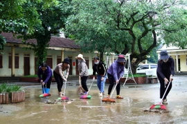 Cán bộ giáo viên Trường Tiểu học Tân Hóa (huyện Minh Hóa, Quảng Bình) vệ sinh khuôn viên trường sau khi nước rút. (Ảnh: Tá Chuyên/ TTXVN)