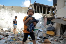 Các em nhỏ thu nhặt đồ đạc sót lại trong đống đổ nát của ngôi nhà bị phá hủy sau cuộc tấn công của Israel vào thành phố Rafah, Dải Gaza ngày 1/5.(Ảnh: THX/TTXVN)