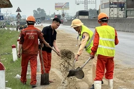 Cảnh sát Giao thông Nghệ An cùng người dân dùng cát, chổi để xử lý số dầu loang. (Ảnh: TTXVN phát)