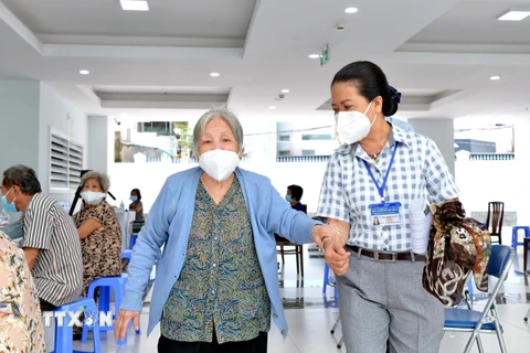 Các y bác sỹ Trung tâm Y tế quận 3, Thành phố Hồ Chí Minh, hỗ trợ, hướng dẫn người trên 65 tuổi, người mắc bệnh mãn tính, người thuộc hộ nghèo tiêm vaccine Moderna phòng COVID-19 đợt 5. (Ảnh: Thanh Vũ/TTXVN)