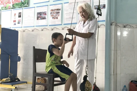 Bà Nguyễn Ngọc Điểu tập luyện phục hồi chức năng vận động cho bé Phan Thanh Phong. (Ảnh: Lê Thúy Hằng/TTXVN)