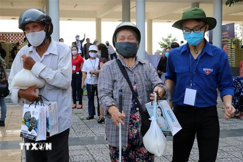Thanh niên tình nguyện hỗ trợ người khiếm thị đi nhận gạo. (Ảnh: Trần Lê Lâm/TTXVN)