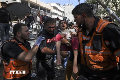 Nhân viên y tế giải cứu một em nhỏ khỏi tòa nhà bị sập sau vụ oanh tạc của máy bay Israel xuống quận Rimal, thành phố Gaza. (Ảnh: AFP/TTXVN)