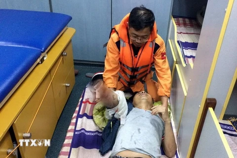 Các y, bác sỹ Trung tâm Phối hợp tìm kiếm cứu nạn hàng hải Việt Nam sơ cấp cứu cho thuyền viên Phạm Văn Thảo trước khi đưa vào đất liền. (Ảnh: Tá Chuyên/TTTXVN)