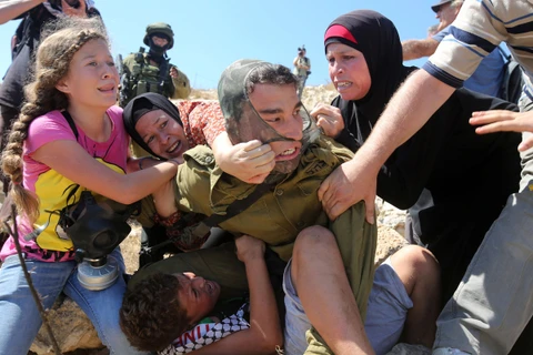 Những phụ nữ Palestine giằng co với một binh sỹ Israel để cứu cậu bé người Palestine trong cuộc biểu tình phản đối Israel tịch thu đất ở khu Bờ Tây. (Ảnh: AFP)