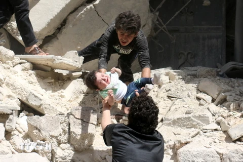 Chuyển một em bé khỏi đống đổ nát sau vụ không kích ở thành phố Aleppo ngày 28/4. (Nguồn: AFP/TTXVN)