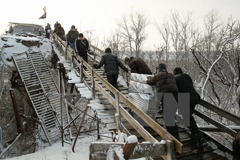 Người dân đi qua chốt kiểm soát giữa quân đội Ukraine và lực lượng đòi độc lập bằng chiếc thang gỗ thay thế cho chiếc cầu bị phá hủy trong một đợt giao tranh ở khu vực Luhansk ngày 16/12. (Nguồn: EPA/TTXVN) 