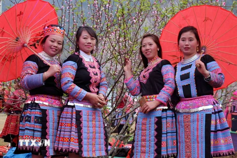 Người con gái Mông trong trang phục truyền thống bên hoa đào. (Ảnh: Diệp Anh/TTXVN)