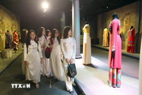 Các em học sinh xem các mẫu áo dài tại triển lãm. (Ảnh: Quang Nhựt/TTXVN)