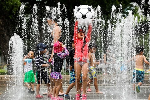 Trẻ em chơi đùa dưới vòi phun nước để tránh nắng nóng tại Tokyo của Nhật Bản ngày 23/7. (Ảnh: EPA/TTXVN)